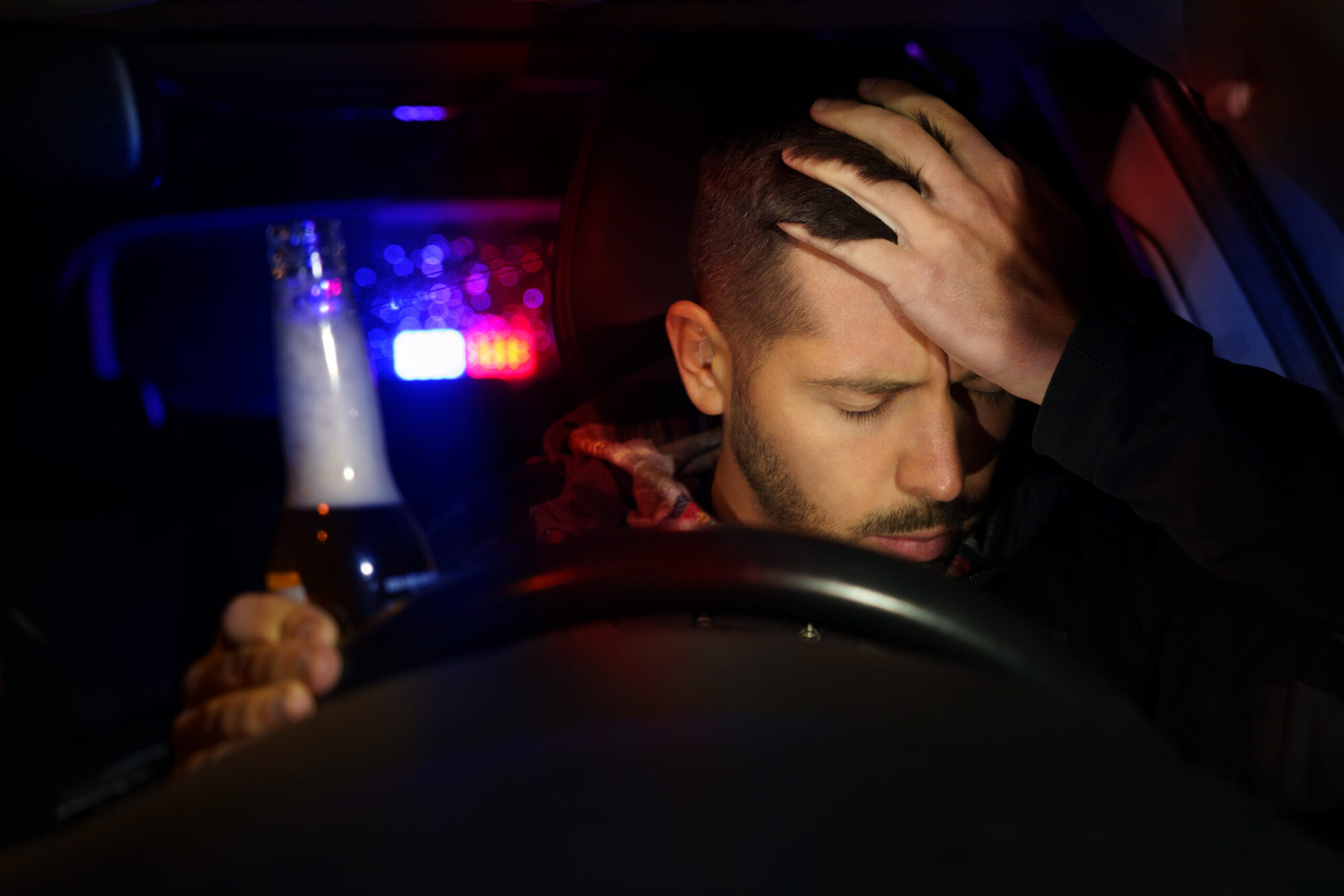 Road police with flashing lights stopped drunk driver. Young man drinking beer while driving car. Driver under alcohol influence. High quality photo